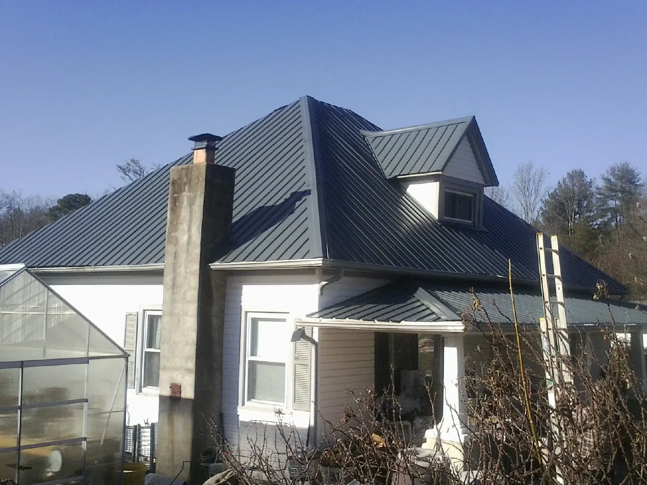 Dark blue standing seam metal roof on a white farmhouse with dormer — Slate & Tile Roof Repair by Roofing Brothers in Ludlow