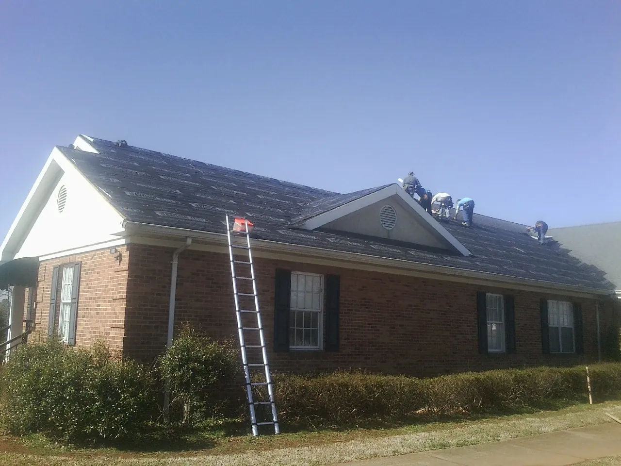 Crew tearing shingles off a brick ranch roof with a ladder set — Metal Roof Repair work by our crew in Ludlow