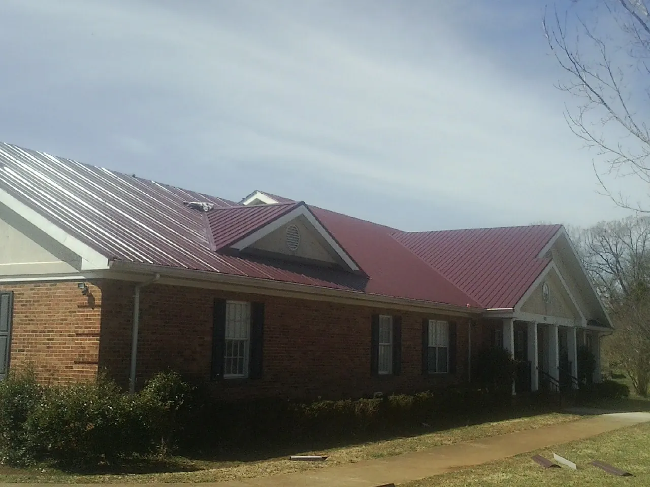 Red metal roof with gabled entries on a long brick building, from a Hail Damage Roof Repair job in Ludlow