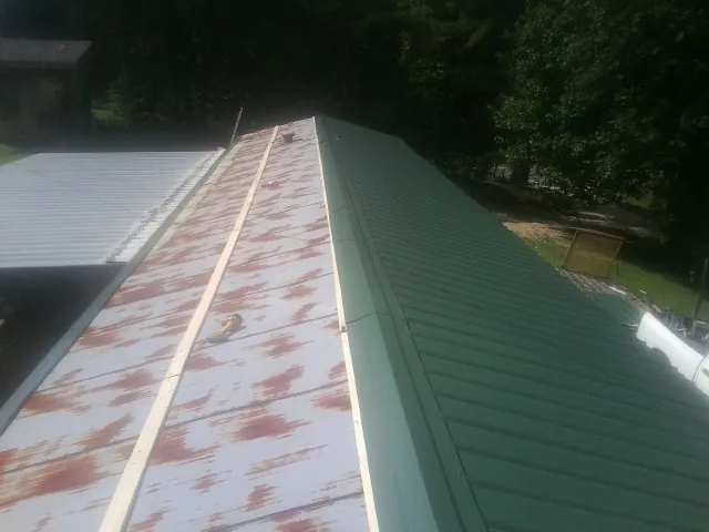 Old rusted panels beside newly installed green metal roofing — Wind Damage Roof Repair by Roofing Brothers in Ludlow
