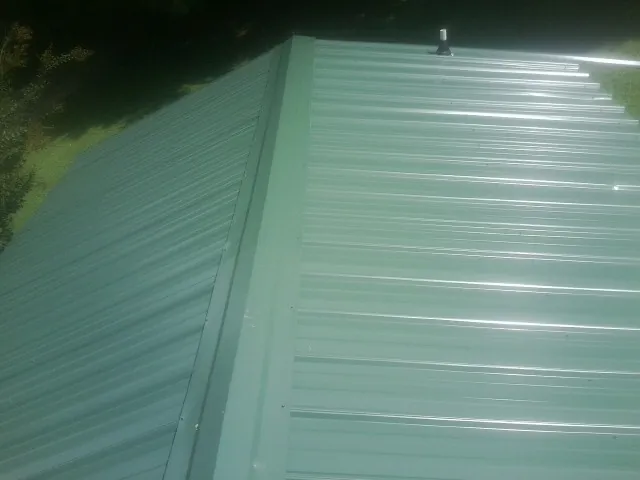 New green metal panels meeting at the ridge of a roof — Flat Roof Repair work by our crew in Ludlow