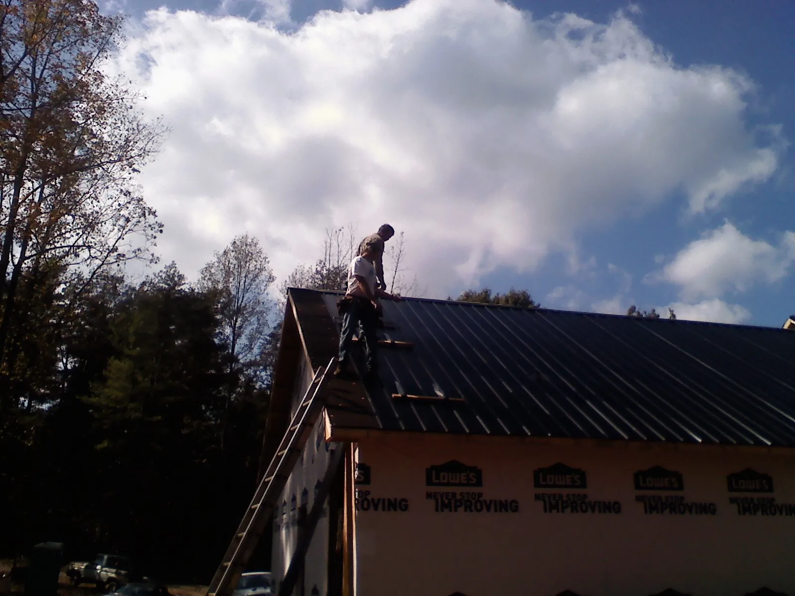 Roofer fastening dark metal panels high against a cloudy sky, from a Roof Inspection job in Ludlow