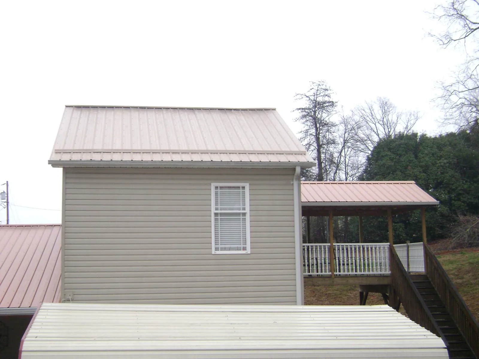 Tan metal roofs on a two story addition and attached porch, from a Roof Replacement job in Ludlow